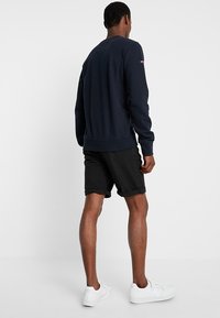 Sudadera azul marino con cuello redondo, puños y dobladillo acanalados. Combinada con pantalones cortos negros. Zapatillas blancas visibles. Diseño sencillo, sin patrones.