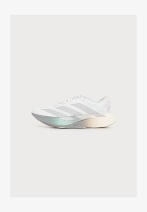 Chaussure de sport blanche avec des rayures gris clair et une semelle épaisse présentant un dégradé du vert argenté au crème, sur un fond uni.