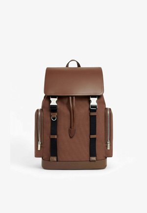 Zaino in tela marrone con patta in pelle, cinghie nere, dettagli in metallo argentato, cerniere laterali e base piatta per stabilità.