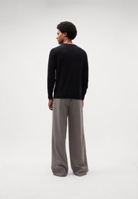 Pulover negru cu mâneci lungi și decolteu rotund, asortat cu pantaloni gri cu pantaloni largi. Texturi fine și design simplu, văzut din spate.
