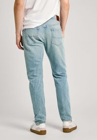 Jeans de mezclilla azul claro con un corte recto, que presentan bolsillos traseros y un parche de cuero en la cinturilla, combinados con zapatillas blancas.