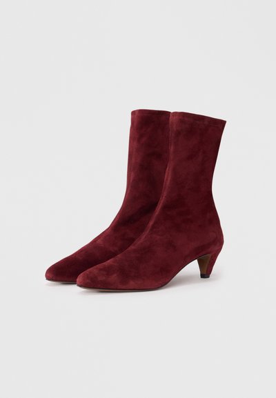 Bottes chevilles en suede bordeaux avec un nez pointu et un talon bas et fin. Texture lisse avec un design épuré.