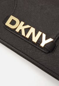 Musta teksturoitu lompakko, jossa on kultainen "DKNY"-logo. Mukana sujuva suljin ja tyylikäs, rakenteellinen muotoilu.