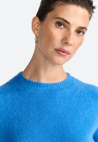 Blå strikket sweater med ribbet rund hals og raglanærmer, lavet af et blødt, tekstureret stof.