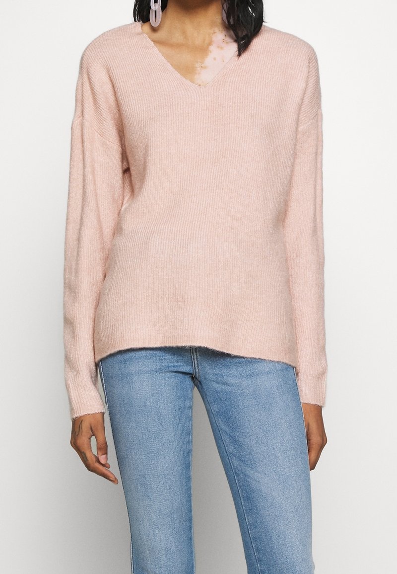 V-ringad ljusrosa tröja med ribbat mönster, avslappnad passform och långa ärmar; bärs med ljusblå skinny jeans.