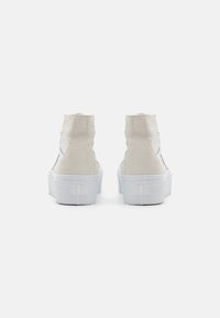 Hoge sneakers met een lichtbeige suede bovenkant, witte rubberen zool en gestikte details aan de zijkanten. Minimalistisch ontwerp.
