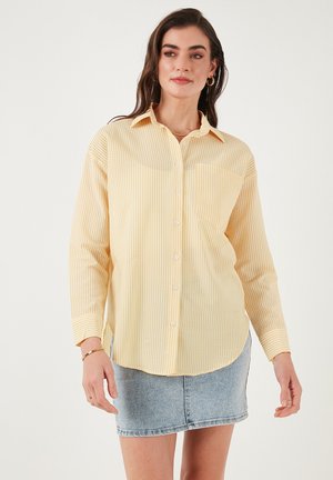 Light yellow striped button-up shirt with long sleeves, a collar, and a single chest pocket, paired with a denim mini skirt.