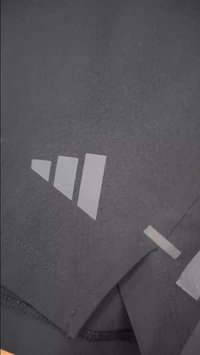 Lähikuva mustasta kankaasta, jossa on kolme valkoista nousevaa palkkia ja pieni vaakasuora valkoinen viiva painettuna.