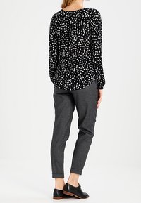 Blouse noire à motif floral blanc, coupe décontractée, manches longues. Pantalon gris texturé avec jambes effilées. Chaussures habillées noires.
