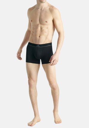 Boxer briefs neri realizzati in tessuto liscio, con un elastico in vita con logo e una forma aderente, indossati da un modello su uno sfondo neutro.