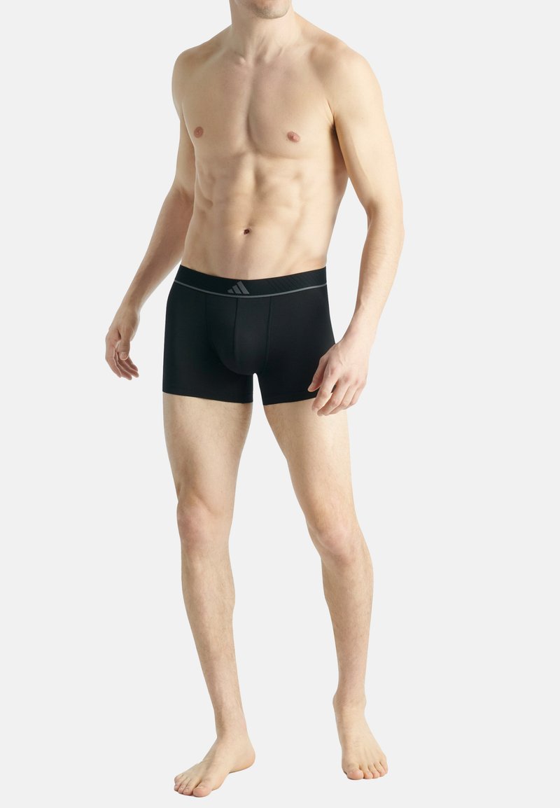 Svarta boxerkalsonger i en mjuk tygkvalitet, med en elastisk midjeband med logotyp och en åtsittande form, visade på en modell med en neutral bakgrund.