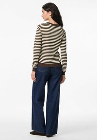 Pruhovaný svetr v hnědé a krémové barvě, kombinovaný s tmavě modrými širokými džíny. Svetr má žebrované manžety a lem. Zobrazená zadní strana.