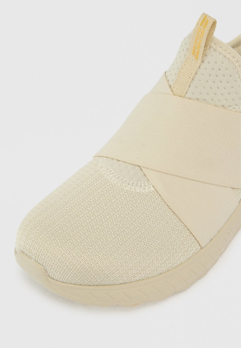 Zapato beis sin cordones con parte superior de malla texturizada, tira elástica en diagonal y punta redonda. Diseño minimalista con suela de goma flexible.