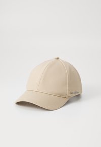 Vaaleanbeige baseball-lippis, joka on valmistettu tekstuuripinnasta ja jossa on kaareva lippa. Lippiksessä on pieni hopea-logo brodeerattuna sivulle.