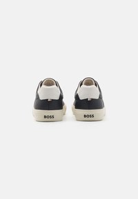 Mustad nahast tossud kreemika aktsendiga, millel on tekstuuriga viimistlus ja kummist taldad. "BOSS" logo on prinditud kontsadele.