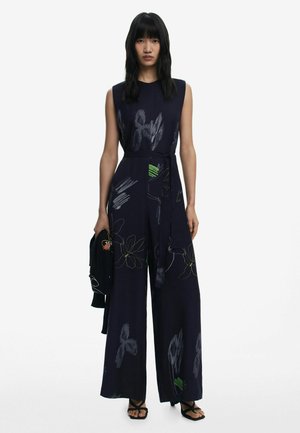 Combinaison en jersey marine sans manches, ornée de motifs floraux verts et blancs. Comprend une ceinture en tissu et une silhouette à jambes larges.