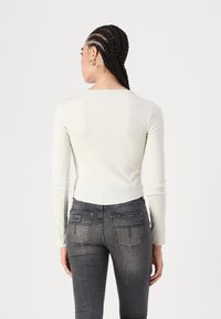 Bijela dugih rukava uska majica s rebrastom teksturom u kombinaciji s tamnosivim skinny trapericama koje imaju stražnje džepove i oznaku branda.
