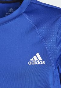 Camiseta deportiva azul hecha de tela ligera con un cuello redondo, que presenta un logo blanco de Adidas y pequeños detalles texturizados.