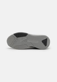 Zapatilla deportiva negra con una suela de goma gris texturizada que presenta patrones de zigzag y un acento triangular en el área del talón.