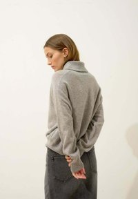 Szary sweter z wysokim kołnierzem, wykonany z miękkiej dzianiny. Posiada długie rękawy i ściągacze, zestawiony z szarym dżinsowym spódnicą.