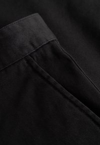 Gros plan sur un tissu noir présentant une texture lisse, des coutures nettement définies et une ceinture pliée, mettant en valeur un design épuré et minimaliste.