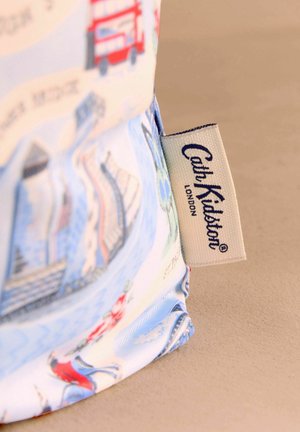 Mėlynas audinio pirkinių maišelis su Londono tema, kuriame pavaizduoti raudoni dviejų aukštų autobusai ir gėlių akcentai. Šone matoma „Cath Kidston“ etiketė.