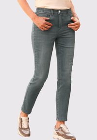 Jean en denim gris avec une coupe slim, doté d'une taille élastique, de poches avant et d'une texture lisse. Associé à des baskets beiges et grises.