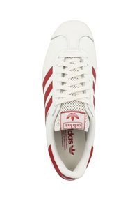 White sneaker with red stripes, lace-up design, perforated toe box, padded tongue, and red logo label on the heel. Flat rubber sole.