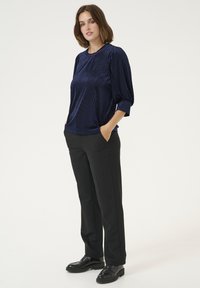 Top in blu navy a coste con collo rotondo e maniche a 3/4, abbinato a pantaloni neri e scarpe nere lucide.