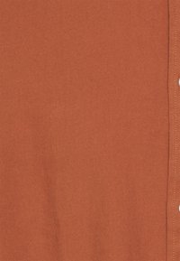 Tissu de couleur rouille avec une texture douce, présentant une patte de boutonnage sur la droite et un motif discret en tissage diagonal.