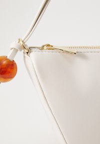 Weißes Lederhandtasche mit einem goldenen Reißverschluss, mit einer glatten Textur und einem dekorativen bernsteinfarbenen Perlenakzent am Riemen.