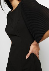 Czarna sukienka z dopasowanym gorsetem i plisowanymi, przezroczystymi rękawami. Sukienka ma gładką fakturę i subtelne detale szwów.