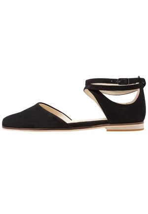 Zapato plano de ante negro con punta afilada, lados cortados y una correa al tobillo con una pequeña hebilla. Revestimiento interior suave y suela plana.