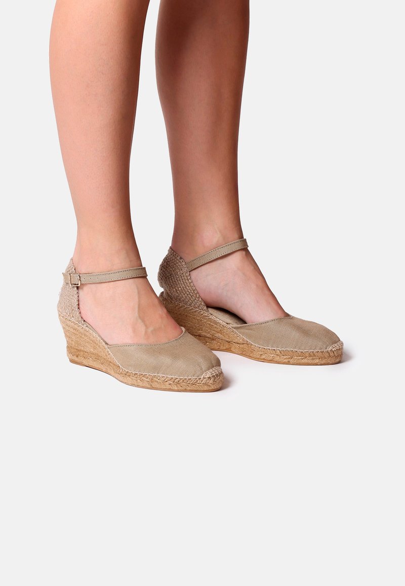 Le zeppe espadrilles beige presentano un corpo in tela e un tacco in juta intrecciata. Un cinturino alla caviglia regolabile tiene fermo il piede con una suola piatta e testurizzata.