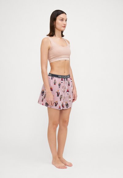 Světlý růžový croptop s logo pásem, spárovaný s červeno-bílými proužkovanými šortkami s barevnými vzory a elastickým pasem.
