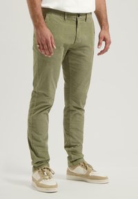 Olívovozelené slim-fit nohavice z bavlny. Majú zapínanie na gombík, pútka na opasok a bočné vrecká. Nosené s béžovými teniskami.