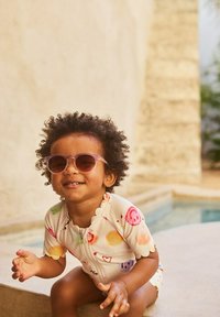 Korte mouwen, meerkleurig badpak met fruitpatronen, ritssluiting en gegolfde randen; kind draagt doorzichtige zonnebril en lacht.