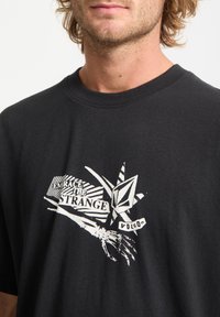 Czarny bawełniany t-shirt z wyrazistym białym nadrukiem z napisami "Przyjmij dziwność" oraz logo, okrągłym dekoltem i krótkimi rękawami.