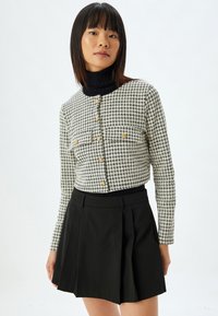 Schwarz-weiße Hahnentrittmuster cropped Jacke mit goldenen Knöpfen, kombiniert mit einem hoch taillierten schwarzen Faltenrock.