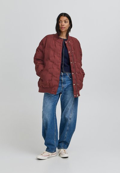 Burgundijas krāsas polsterēta bomber jaka ar apģērba izgriezumu, pogām un kabatām, kombinēta ar gaiši ziliem platām kājām džinsiem un baltām sporta apaviem.