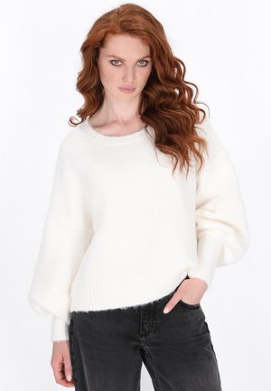 Weißer, flauschiger Pullover mit rundem Ausschnitt und langen, ballonförmigen Ärmeln, kombiniert mit schwarzen Jeans. Weicher Stoff und lockere Passform.