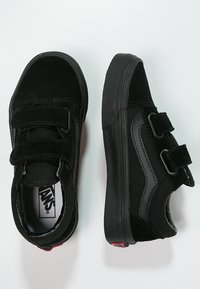 Black low-top sneakers with suede and fabric upper, dual Velcro straps, rubber sole, and contrasting red heel detail.