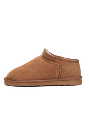 Mocassin en daim marron avec un bout rond, un revêtement intérieur doux, une hauteur de cheville basse et une semelle en caoutchouc texturée, présentant des détails de couture subtils.