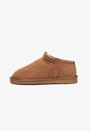 Mocassin en daim marron avec un bout rond, un revêtement intérieur doux, une hauteur de cheville basse et une semelle en caoutchouc texturée, présentant des détails de couture subtils.