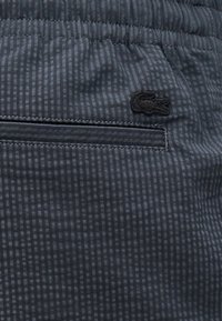 Shorts en tissu bleu marine avec un motif à carreaux subtil, taille élastique, et un petit logo Lacoste noir sur la poche arrière.