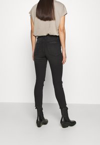 Svarta skinny jeans med fransade fållar, högmidjade, i kombination med en beige kortärmad topp. Svarta ankelstövlar fullständiggör outfiten.