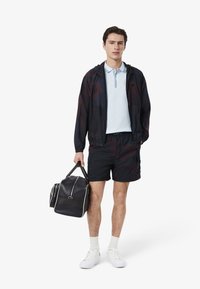 Lätt svart vindjacka, blå pikétröja, svarta shorts, vita sneakers och en mörk duffelväska med vita detaljer.