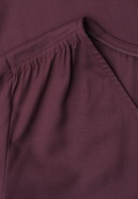 Gros plan d’un vêtement violet montrant un détail de tissu froncé le long de la couture de l’épaule et un col arrondi.