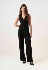 Juodas berankovis liemuo su priekiniais mygtukais, derinamas su aukšta juosmens plataus kirpimo kelnėmis. Lygi tekstūra ir pritaikytas siluetas. Aukšti kulniukai.