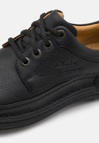 Black leather shoe featuring round laces, metal eyelets, and stitched detailing on the side. Inside has a tan lining for contrast.